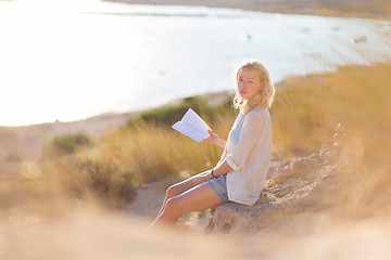 Image showing Woman enjoys reading on beautiful sandy beach.