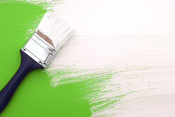 Image showing Paintbrush with white paint painting over green