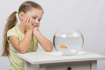 Image showing Four-year girl is looking at a goldfish in an aquarium