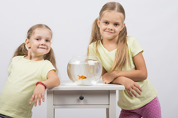 Image showing Two sisters stand at the small fishbowl with goldfish