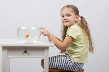 Image showing Four-year girl sitting in front of an aquarium with goldfish and knocks his finger on it