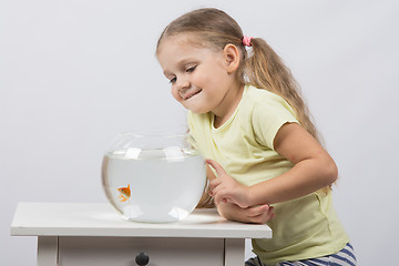 Image showing Four-year girl smiling looking at a goldfish in an aquarium