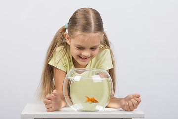 Image showing Happy six year old girl looking down on the aquarium with goldfish