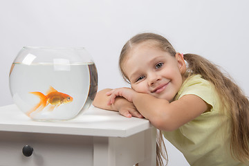 Image showing Happy four-year girl put her head in his hands sitting in front of a goldfish