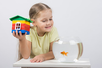 Image showing The four-year girl sits with a toy house in front of a goldfish