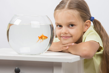 Image showing Six year old girl put her head on the handle sitting at the table with an aquarium with goldfish