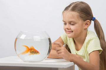 Image showing Happy little girl knocking his finger on the aquarium with goldfish