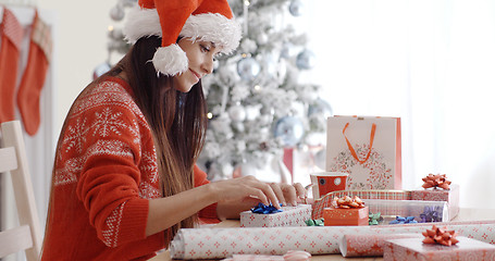 Image showing Young woman sitting wrapping Christmas gifts