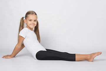 Image showing Girl gymnast sitting on the floor with legs stretched and leaned back on his hands