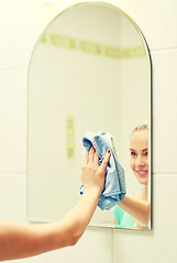 Image showing close up of happy woman cleaning mirror with rag