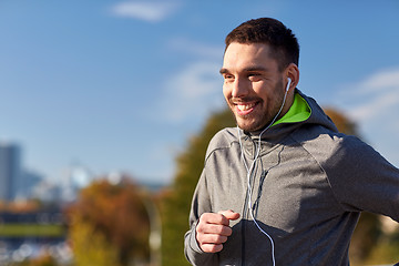 Image showing happy man with earphones running in city