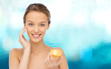 Image showing happy young woman applying cream to her face