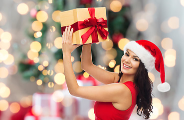 Image showing happy woman in santa hat with gift over lights