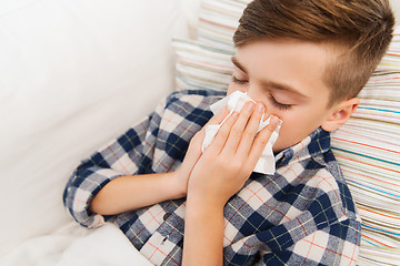 Image showing ill boy lying in bed and blowing his nose at home