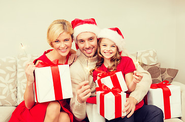 Image showing smiling family holding gift boxes and sparkles