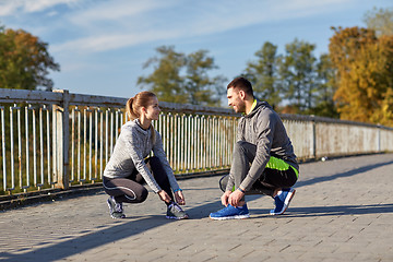 Image showing smiling couple tying shoelaces outdoors