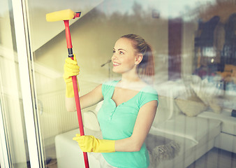 Image showing happy woman in gloves cleaning window with sponge
