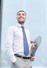 Image showing young smiling businessman with skateboard outdoors