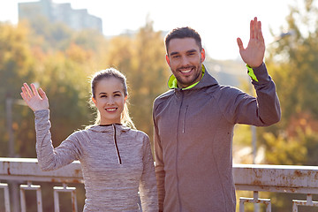 Image showing smiling couple waving hand outdoors