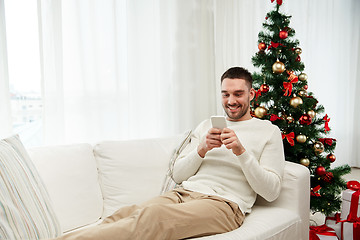 Image showing smiling man with smartphone at home for christmas