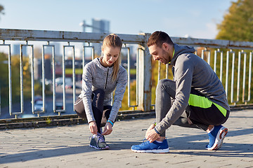 Image showing smiling couple tying shoelaces outdoors