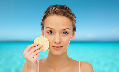 Image showing young woman cleaning face with exfoliating sponge