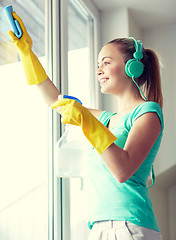 Image showing happy woman with headphones cleaning window