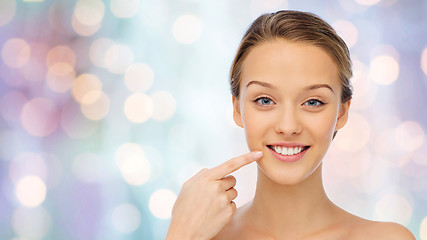 Image showing happy young woman pointing finger to her teeth