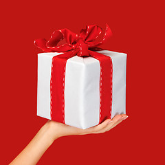 Image showing close up hand holding christmas gift box over red