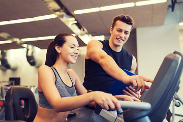 Image showing happy woman with trainer on exercise bike in gym