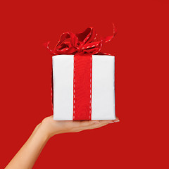 Image showing close up hand holding christmas gift box over red