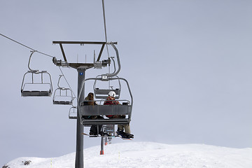 Image showing Snowboarders on chair-lift and ski slope at gray day