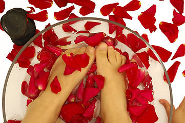 Image showing Feet of child in spa with rose petals and stone