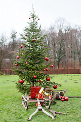 Image showing Old wooden frame a sledge with Christmas parcels before a decorated Christmas tree