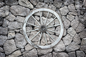 Image showing Wooden wagon wheel on a stone back ground.