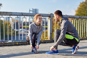 Image showing smiling couple tying shoelaces outdoors