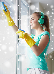 Image showing happy woman with headphones cleaning window