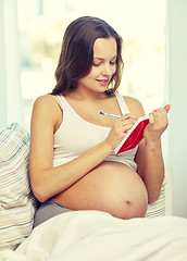 Image showing happy pregnant woman writing to notebook at home