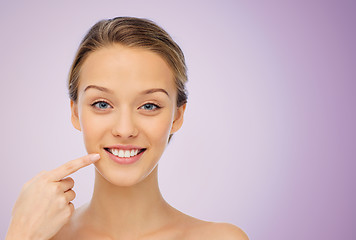 Image showing happy young woman pointing finger to her smile