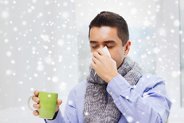 Image showing ill man with flu drinking tea and blowing nose