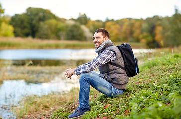 Image showing smiling man with backpack resting on river bank