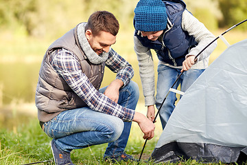 Image showing happy father and son setting up tent outdoors