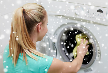 Image showing happy woman putting laundry into washer at home