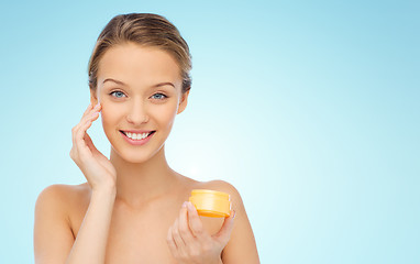 Image showing happy young woman applying cream to her face