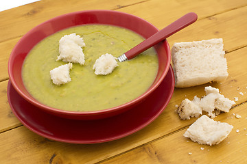 Image showing Torn pieces of bread on green pea and ham soup in a red bowl