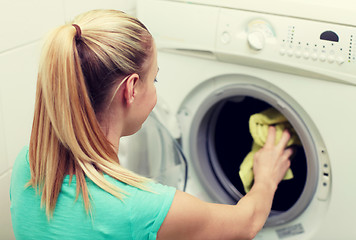 Image showing happy woman putting laundry into washer at home