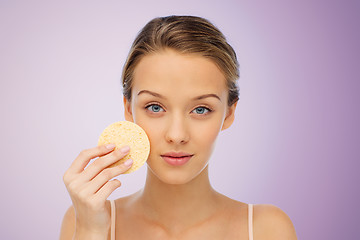 Image showing young woman cleaning face with exfoliating sponge