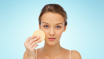 Image showing young woman cleaning face with exfoliating sponge