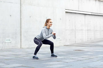 Image showing happy woman doing squats and exercising outdoors