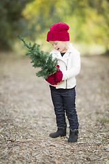 Image showing Baby Girl In Red Mittens and Cap Holding Small Christmas Tree